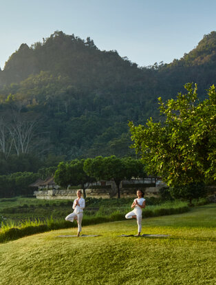 Two people practising yoga on a lawn overlooking a valley at Amanjiwo, Java, Indonesia.