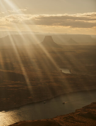 Aerial view of desert landscape with sunlight streaming through clouds over a winding river below, from a private air tour at Amangiri resort.