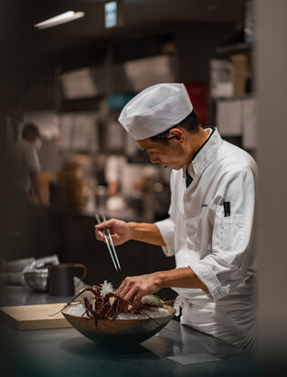 Chef preparing a dish at Amanemu, Japan, with focused attention to culinary detail.