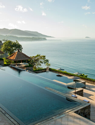 安缦丘澜度假村的水边住宅，无边际泳池俯瞰平静海湾和远处山景。