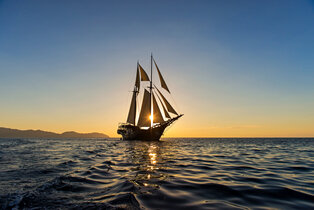 Traditional sailing vessel at dusk near Amandira, Indonesia, silhouetted against golden water.