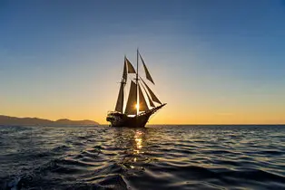 Traditional sailing vessel at dusk near Amandira, Indonesia, silhouetted against golden water.