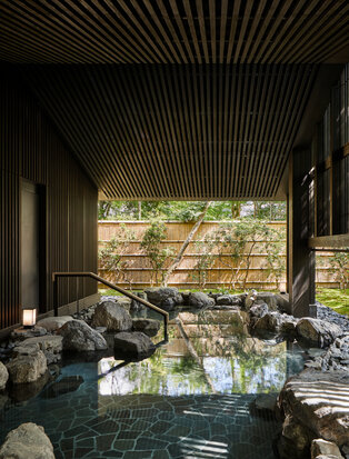 Outdoor onsen at Aman Kyoto with natural rock pool, wooden slatted ceiling and garden views.