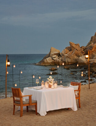 Private dining setup on Amanoi's beach at sunset, with table beside rocky coastline.