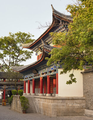Traditional Chinese architecture with curved roof at Amandayan, framed by lush green foliage.