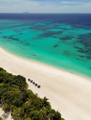 Aerial view of a white sand beach and turquoise waters at Amanpulo, Philippines, with tropical vegetation along the shoreline.
