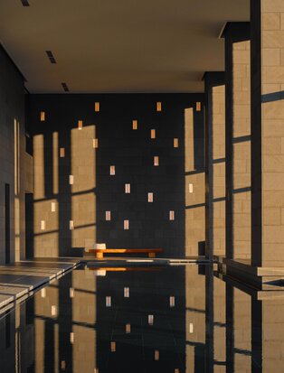Spa pool at Aman Tokyo with warm lighting reflecting off still water, framed by wooden architectural elements.