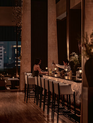Candlelit dining setup at Aman Nai Lert Bangkok with wooden chairs, floral arrangements, and warm evening ambiance.