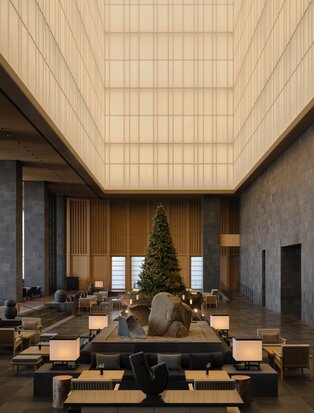 Aman Tokyo lobby at Christmas, with illuminated coffered ceiling above dining tables decorated with evergreen arrangements.