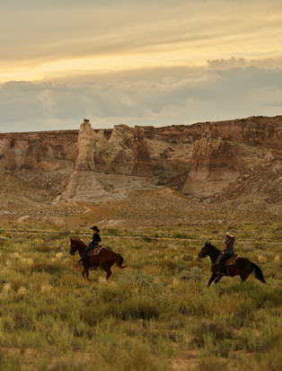Two riders on horseback across desert grassland at Amangiri, Utah.