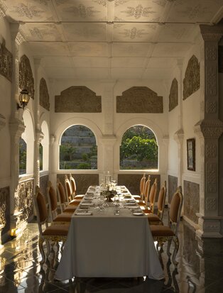 Royal dinner setup at Amankila, Karangasem, with candlelit table beneath arched ceiling and garden views.