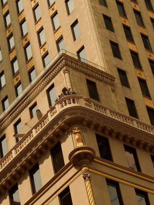 Architectural detail of a classical stone building corner at Aman New York hotel, with ornate moulding and rows of windows.
