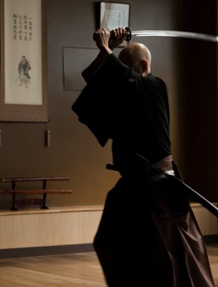 Iaido swordsman in traditional black hakama and gi demonstrating sword technique at Aman Tokyo.