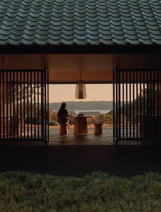 Amanemu's Welcome Pavilion at dusk, wooden screens framing illuminated interior with traditional Japanese architecture.