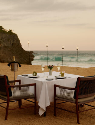 Private dining table set on a beach terrace at Amanera, Dominican Republic, overlooking the ocean at dusk.