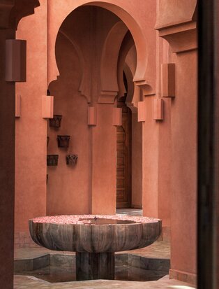 Terracotta-toned arched doorway with central fountain at Amanjena, Morocco.
