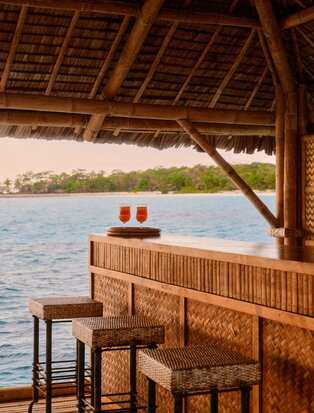 Floating bar at Amanpulo overlooking calm Philippine waters, with wooden counter and seating beneath thatched roof.