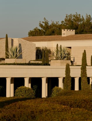Amanzoe resort exterior with cypress trees and contemporary stone architecture at dusk, Greece.