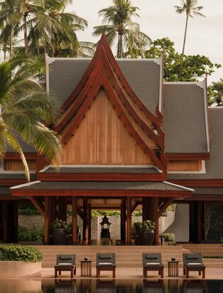 Amanpuri's arrival pavilion reception displaying traditional Thai architectural design with peaked wooden roof and palm trees.