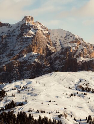 Skiers and snowboarders on snow-covered slopes beneath dramatic Alpine peaks at Aman Rosa Alpina, Italy.