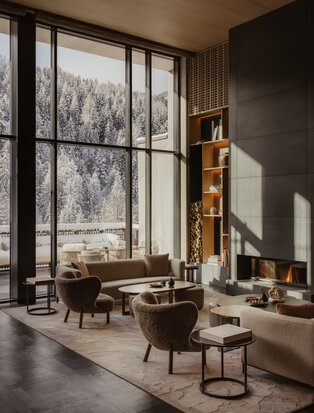Sunlit lounge at Aman Rosa Alpina with mid-century furniture and Alpine views through tall windows.