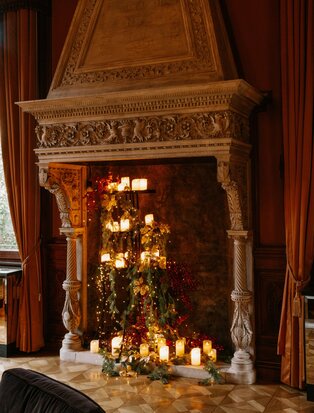 Ornate wooden fireplace mantelpiece decorated with evergreen garland and candlelight at Aman Venice.