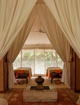 Spa interior at Aman-i-Khas with draped fabric entrance, two terracotta chairs, and large window overlooking gardens.