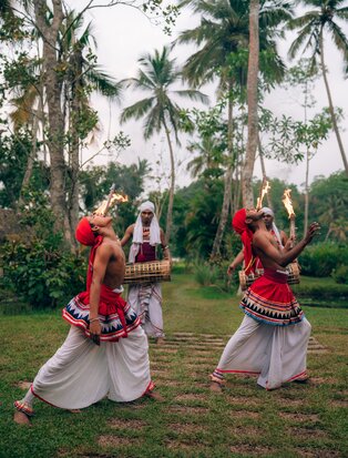 Two women in traditional Sri Lankan dress dancing on a palm-lined lawn at Amangalla during a private dinner entertainment event.