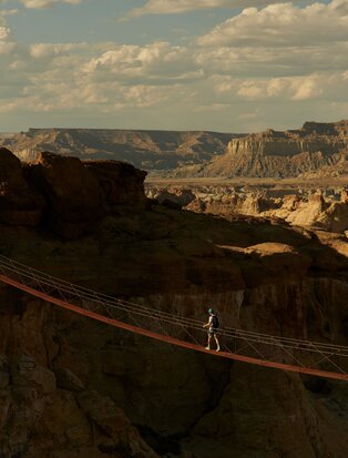 Personne traversant un pont suspendu lors d'une via ferrata à Amangiri, avec des formations rocheuses désertiques en arrière-plan.