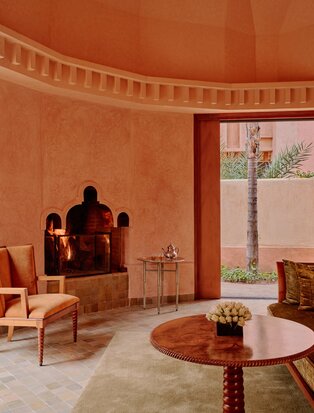 Amanjena pavilion interior with terracotta walls, curved fireplace, and circular dining table.
