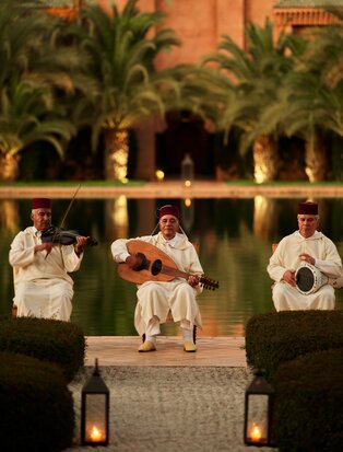 Musicians performing traditional Moroccan music at Amanjena at dusk, framed by illuminated palms.
