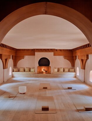 Amanjena's yoga studio with terracotta arches, wooden beams and meditation cushions on a light stone floor.
