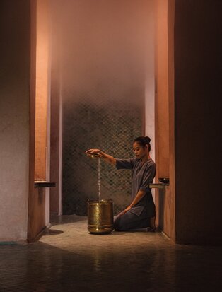 Woman seated in meditative pose within warmly lit doorway at Amanjena spa, Morocco.