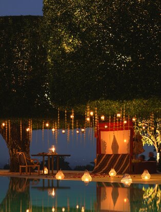 Candlelit Javanese wayang dinner setup at Amanjiwo, with glowing lanterns reflected in still water at dusk.