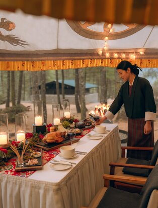 Forest and Fortress dinner setup at Amankora, Paro, with long table decorated with candles and foliage beneath wooden ceiling.