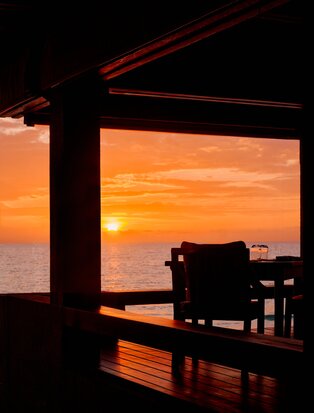Silhouetted pavilion with dining furniture framing an orange sunset over the Philippine sea at Amanpulo.