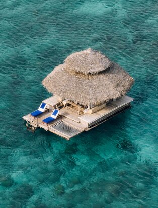 Floating Kawayan Bar at Amanpulo, Philippines, with thatched roof structure on wooden platform in turquoise waters.
