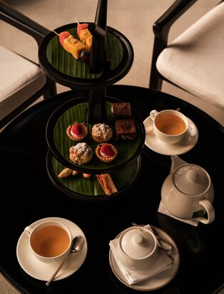Afternoon tea service at Amansara with tiered stand, pastries and teacups arranged on dining room table.