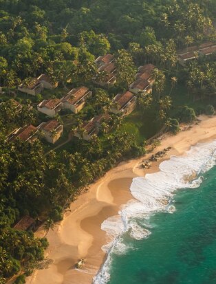 Aerial view of Amanwella's sandy cove bordered by emerald waters and dense tropical forest, Sri Lanka.
