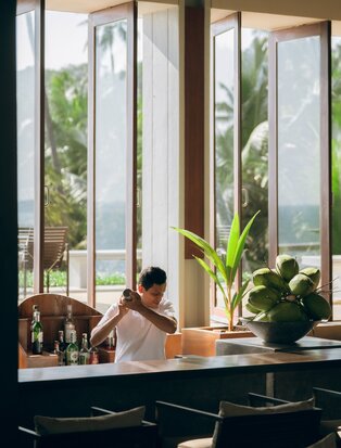 Woman relaxing by floor-to-ceiling windows at Amanwella's lounge bar in Sri Lanka.