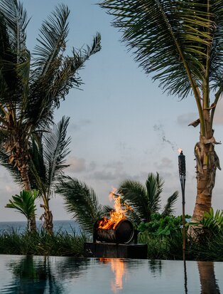 Bonfire reflected in still water at dusk, framed by palm trees at Amanera, Dominican Republic.