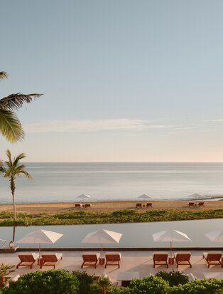 Amanvari's main pool at sunset, with palm trees and ocean view beyond.