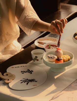 Hands holding brush over ceramic plates during afternoon tea at Amanyangyun, China.