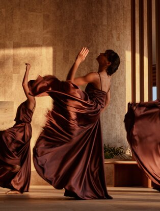 Dancer in burgundy silk robes mid-movement at Amanvari resort, warm lighting casting dramatic shadows.