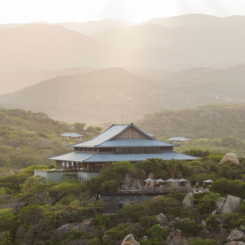 Amanoi resort's distinctive blue-roofed pavilion nestled among verdant hillsides at dawn.