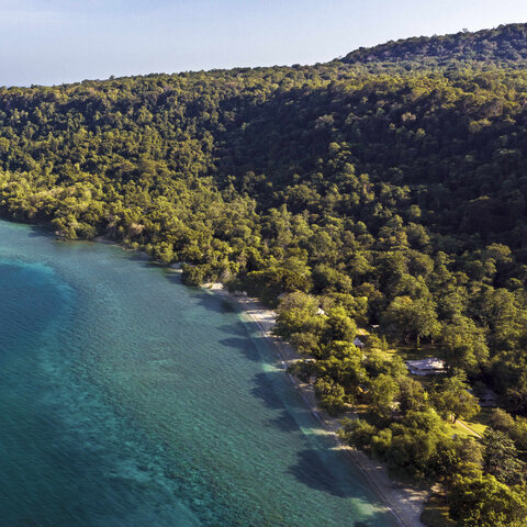 Aerial view of Amanwana on Moyo Island with turquoise waters and dense tropical forest coastline.