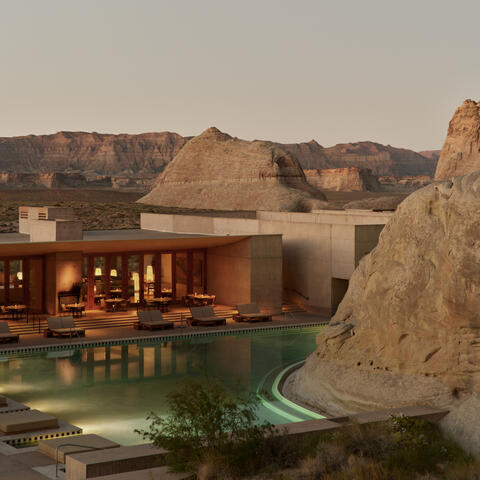 Amangiri exterior at dusk with illuminated pavilions, reflecting pool and desert rock formations.