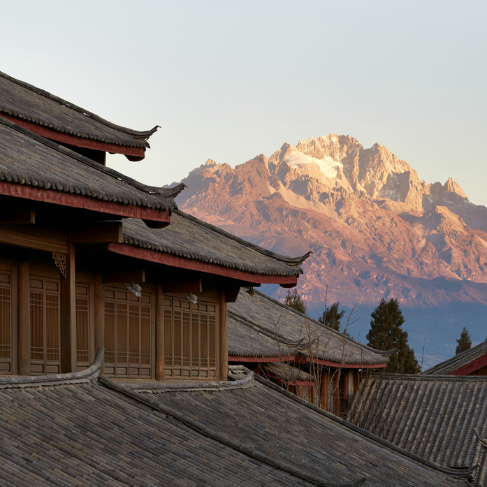 Amandayan's wooden pavilions with curved roofs frame a snow-capped mountain at sunrise.