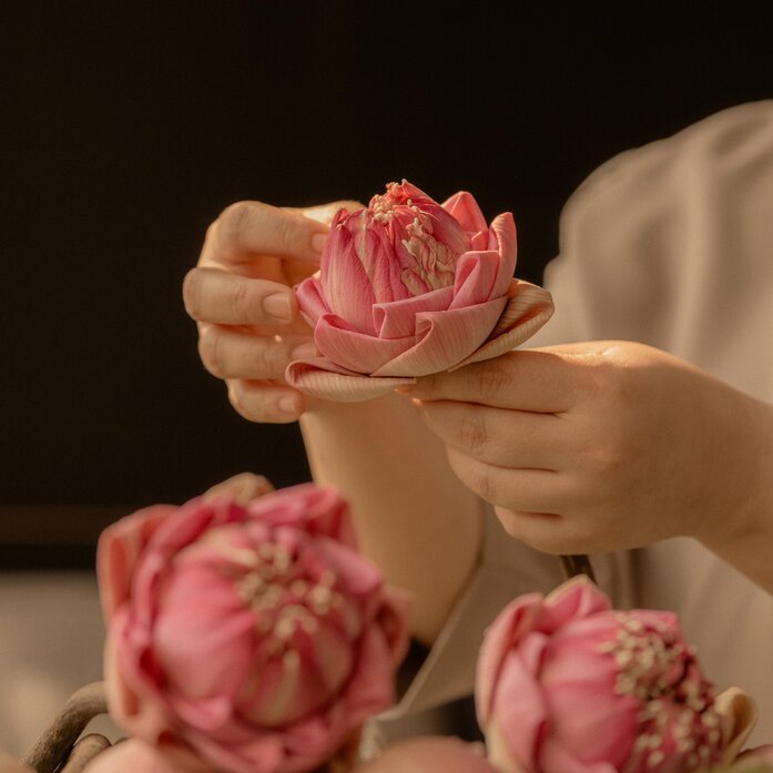 Pink lotus flowers cradled in hands at Aman Nai Lert Bangkok.