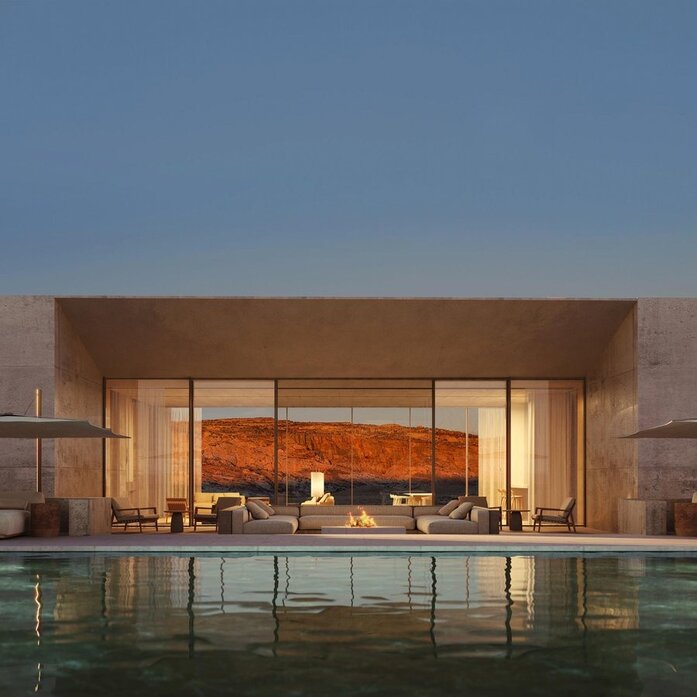 Amangiri residence with illuminated interior viewed across reflecting pool at dusk.